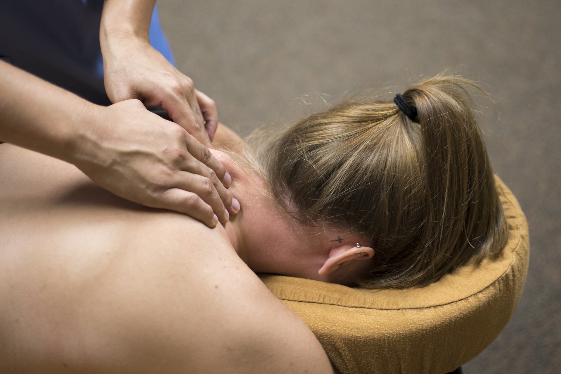 head and shoulder shot of a woman lying face down on a massage couch her head in a cradle and she is getting a neck massage