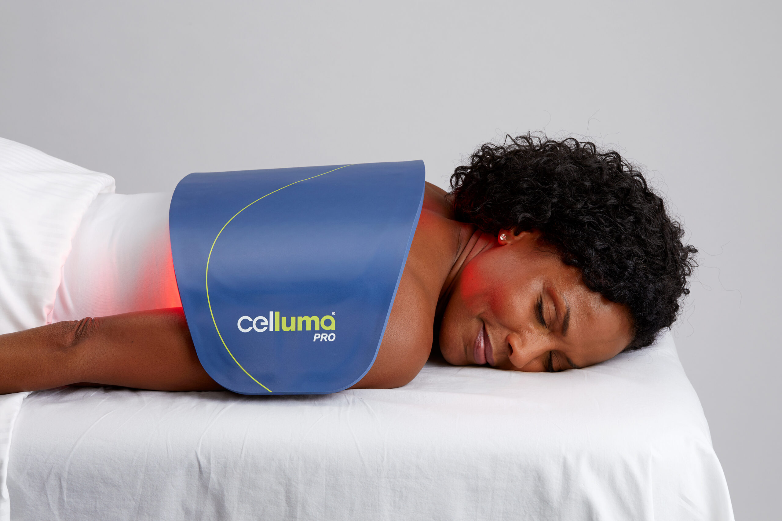 picture of top half of black woman lying down on a white massage couch with the celluma pro light therapy device across her back
