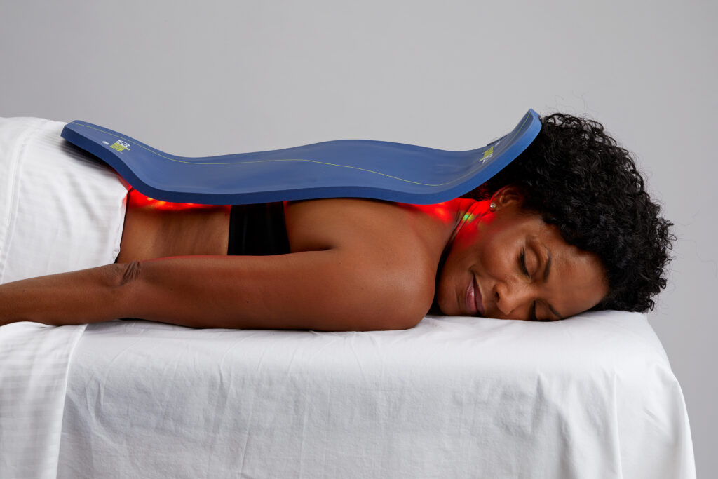 top half of a lady lying down on her front on a white massage couch with the Celluma LED Light therapy device laid upon her back