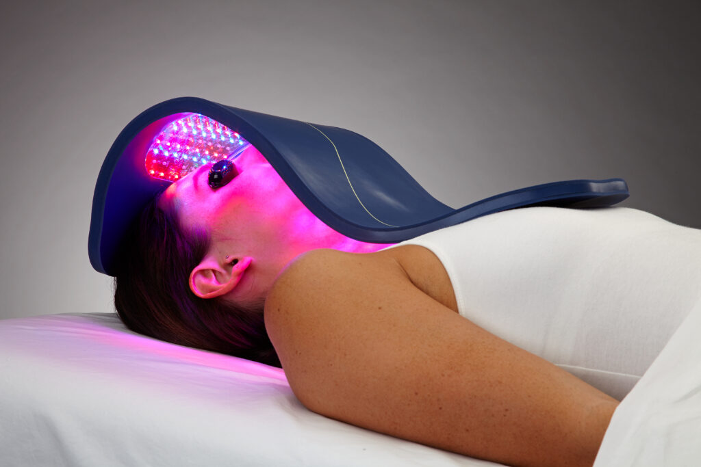 woman lying down on her back, top half showing only, with the Celluma LED light therapy device over her face and neck